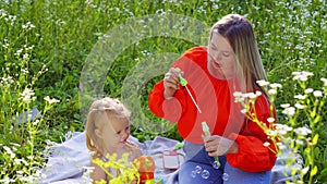 Mother and daughter, in the middle of daisies, blow soap bubbles.