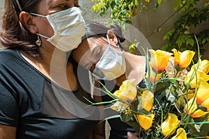 Mother and daughter mourning those lost to the coronavirus, wearing face masks, showing mutual support, hugging