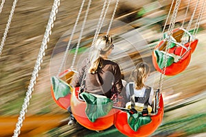 Mother with daughter moving fast on carousel. Motion blur captured, focused on bodies
