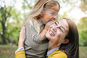 Mother and daughter outdoors in a meadow. Daughter whispering to photo