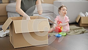 Mother and daughter packing cardboard box playing on floor at new home