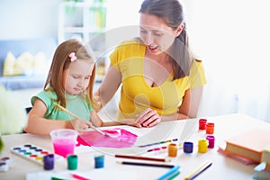 Mother daughter paints watercolor on a sheet of paper sitting at home at the table in a bright room