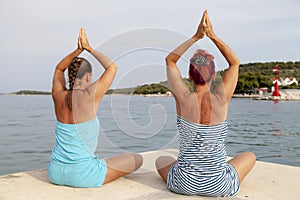 Mother and daughter performing joga on sunny beach