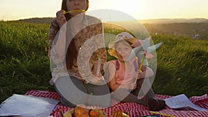 Mother and daughter on a picnic on a hill in the summer at sunset.