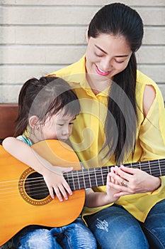 Mother with daughter play guitar. Family spending time together