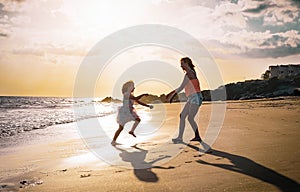 Mother and daughter playing on the beach at sunset - Happy family having fun in vacation on the beach