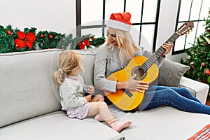 Mother and daughter playing guitar and singing sitting by christmas tree at home