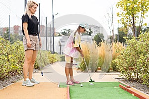 mother and daughter playing mini golf, children enjoying summer vacation