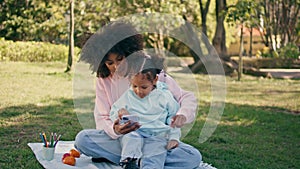 Mother daughter playing telephone on grass meadow. Woman showing phone to girl