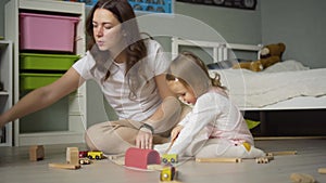 Mother and daughter playing together with toys indoor at home. Mom helps her baby girl. Family lifestyle concept