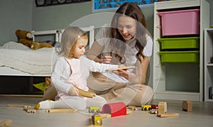 Mother and daughter playing together with toys indoor at home. Mom helps her baby girl. Family lifestyle concept