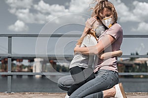 mother and daughter in protective masks hugging on bridge air