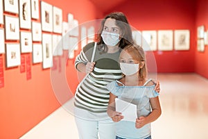 Mother and daughter in protective medical masks looking at expositions in museum