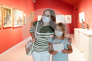 Mother and daughter in protective medical masks looking at expositions in museum