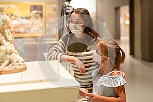 Mother and daughter in protective medical masks looking at expositions in museum