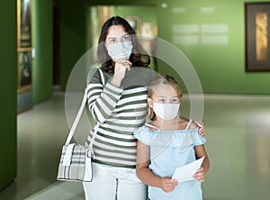 Mother and daughter in protective medical masks looking at expositions in museum