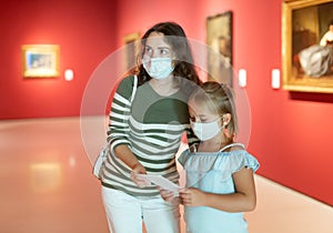 Mother and daughter in protective medical masks looking at expositions in museum