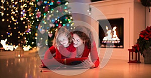 Mother and daughter read a book at fireplace on Christmas eve.