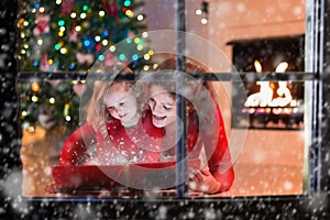 Mother and daughter read a book at fireplace on Christmas eve.