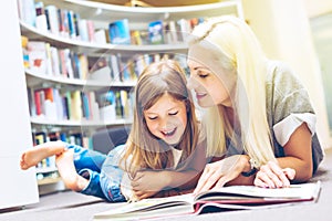 Mother with daughter read book together in library