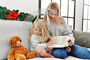 Mother and daughter reading book sitting by christmas decor at home