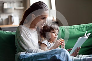 Mother and daughter reading book sitting on sofa at home