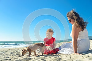 Mother and daughter in red dress and dog on the beach