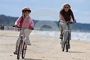 Mother and daughter riding along the beach