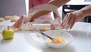 Mother and daughter rolling out flour dough at table closeup