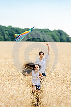 Mother and daughter run in a wheat field with a kite in the summer. Well-planned and active weekend. Happy childhood.