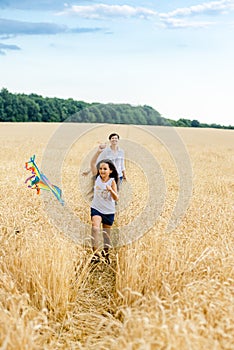 Mother and daughter run in a wheat field with a kite in the summer. Well-planned and active weekend. Happy childhood.