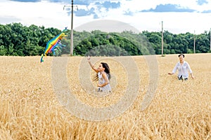 Mother and daughter run in a wheat field with a kite in the summer. Well-planned and active weekend. Happy childhood.