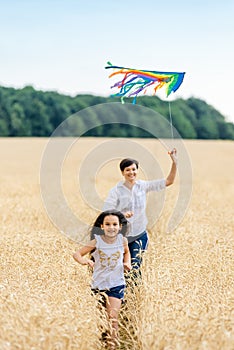 Mother and daughter run in a wheat field with a kite in the summer. Well-planned and active weekend. Happy childhood.