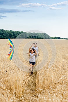 Mother and daughter run in a wheat field with a kite in the summer. Well-planned and active weekend. Happy childhood.