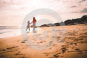 Mother and daughter running along the seashore at sunset - Happy family having fun playing together in tropical sea destination