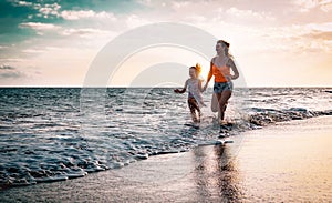 Mother and daughter running along the seashore at sunset - Happy family having fun playing together in vacation on the beach