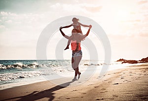 Mother and daughter running together along the seashore on the beach - Happy family piggyback at sunset