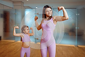 Mother and daughter shows the muscles in gym