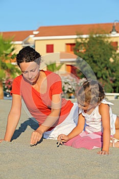 Mother with daughter sit on beach and draw on sand