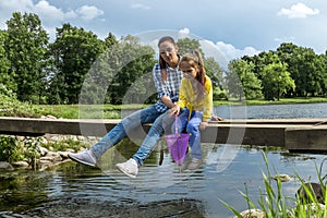 A mother and daughter sit on a bridge across a river on a  summer day