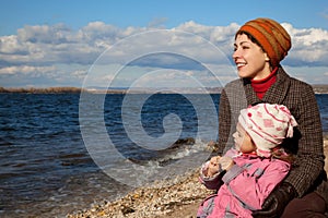 Mother and daughter sit near lake and look