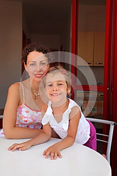 Mother with daughter sit on verandah near table photo