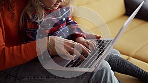 Mother and daughter sitting on the couch, typing on laptop keyboard