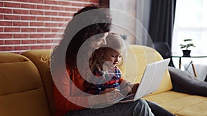 Mother and daughter sitting on the couch and typing on laptop together