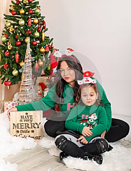 Mother and daughter sitting down in front of christmas tree