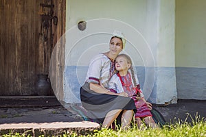 mother and daughter are sitting near the house in Ukrainian folk dresses