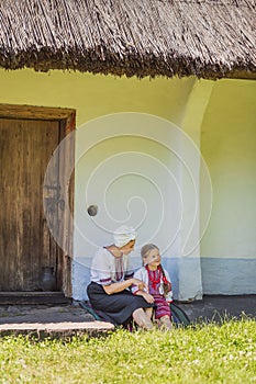 mother and daughter are sitting near the house in Ukrainian folk dresses