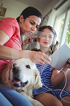 Mother and daughter sitting with pet dog and using digital