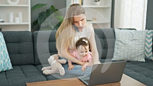 Mother and daughter sitting on sofa talking on smartphone using laptop stressed at home