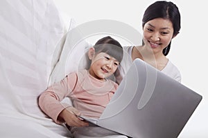 Mother and daughter sitting on sofa using a laptop, tilt